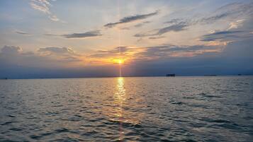 Um pôr do sol sobre um mar calmo, com um cais ao longe.