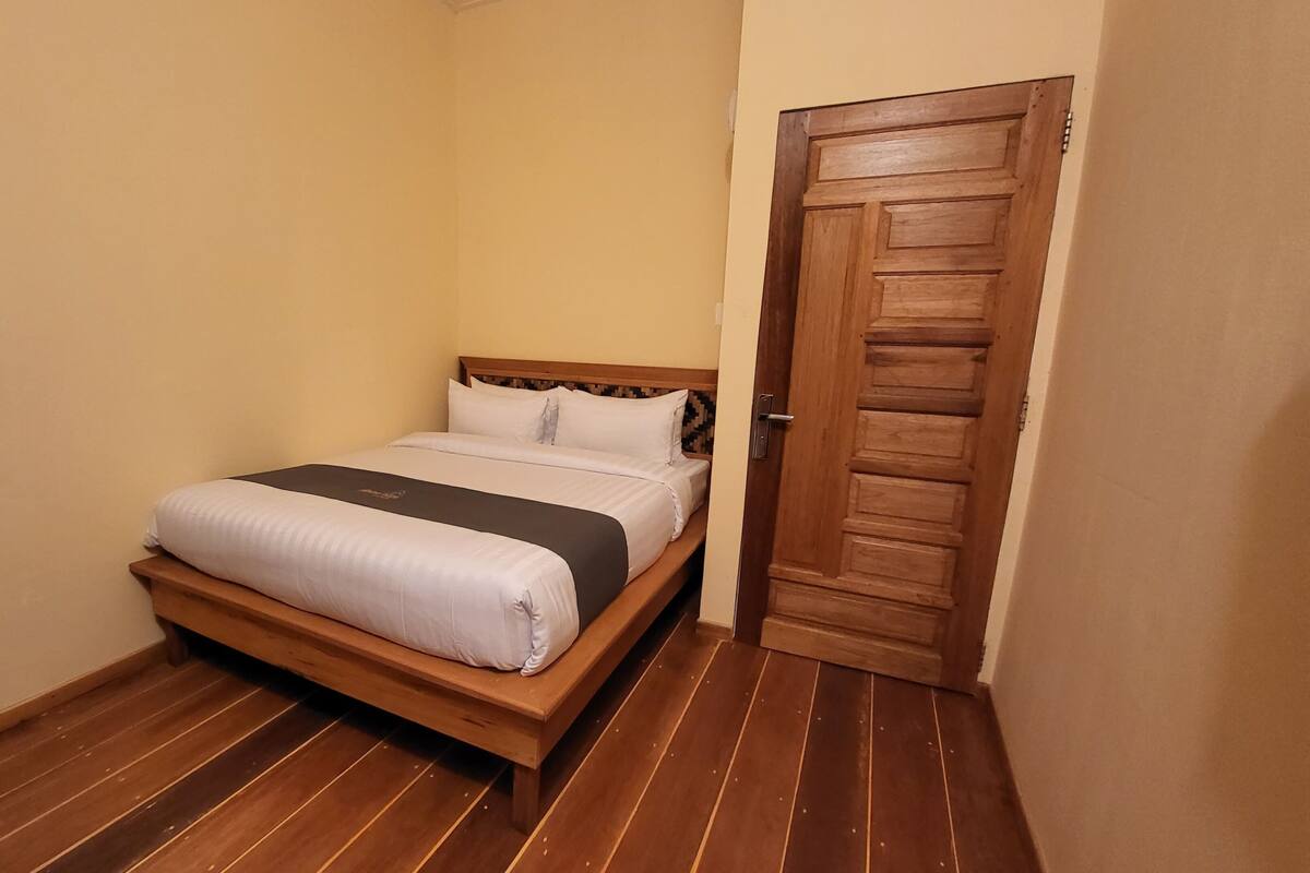 Een klein, netgemaakt bed in een kamer met houten vloeren en een houten deur.