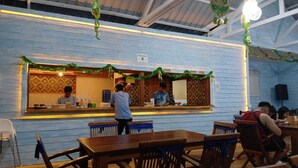 An indoor dining area with wooden tables and chairs, a counter with a person serving, and festive decorations.