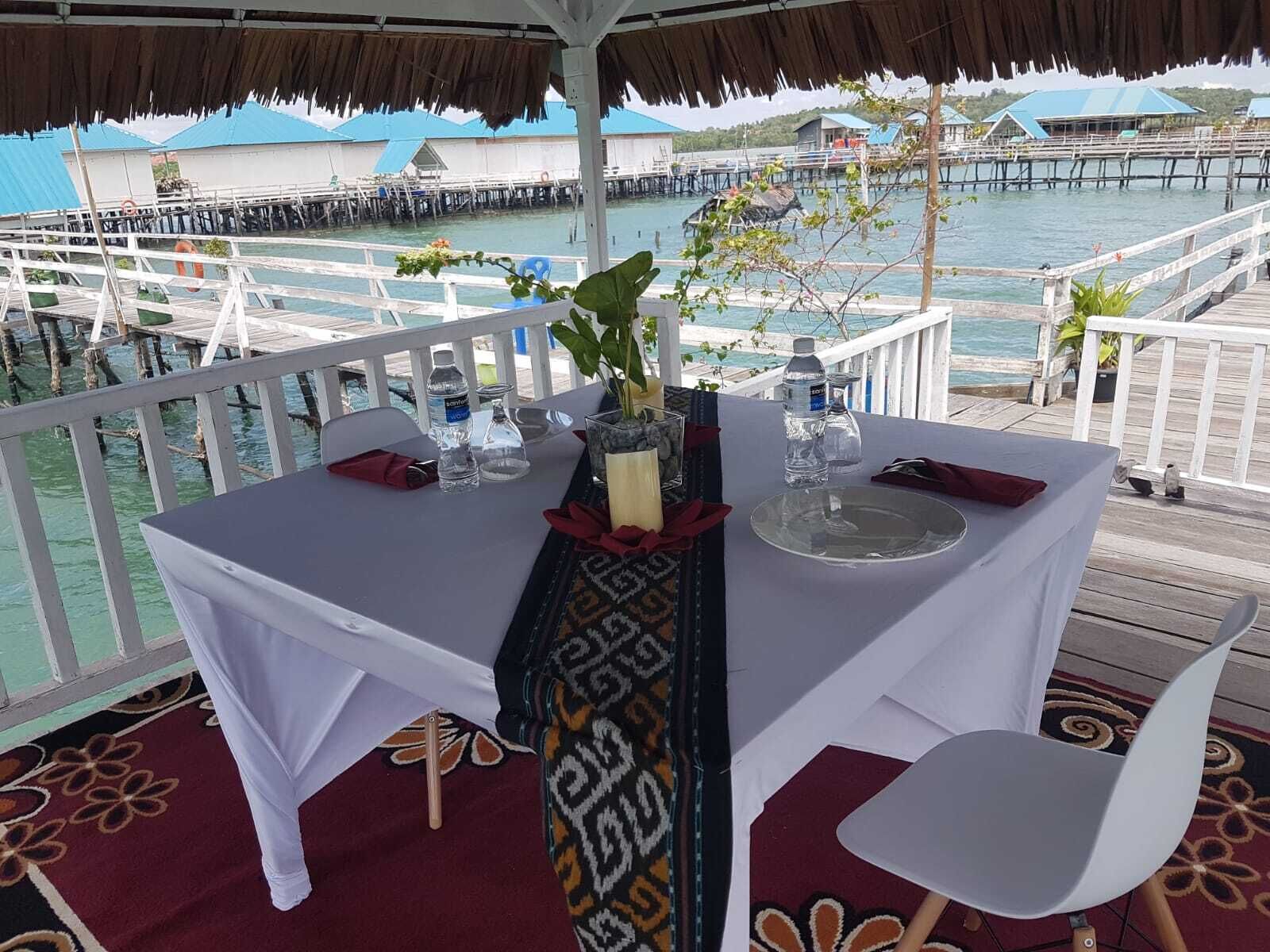 A table set for two with a view of overwater bungalows and a pier.