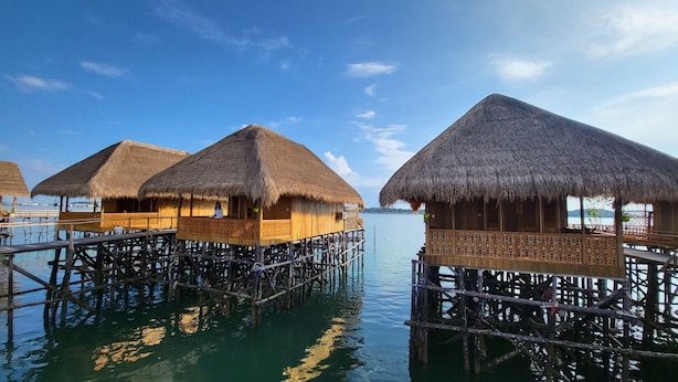 Overwater bungalows with thatched roofs and wooden railings, connected by walkways over calm water.