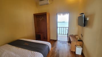 A bedroom with a bed, a wooden wardrobe, a television, a small desk, and a view of a body of water.