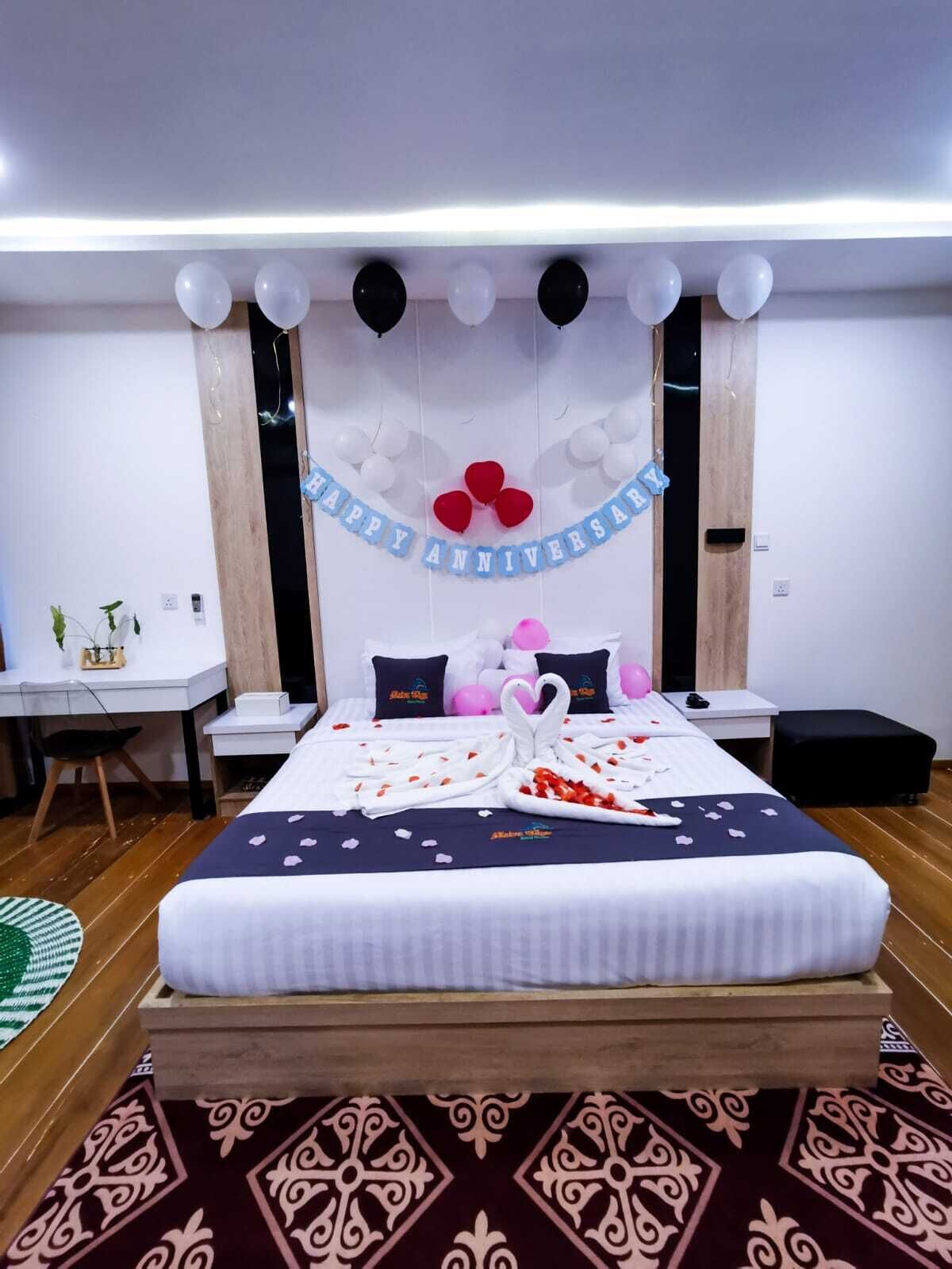 A hotel room with a bed, a desk, and a chair. There is a banner on the wall that says "Happy Anniversary".