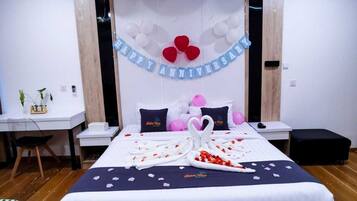 A hotel room with a bed, a desk, and a chair. There is a banner on the wall that says "Happy Anniversary".