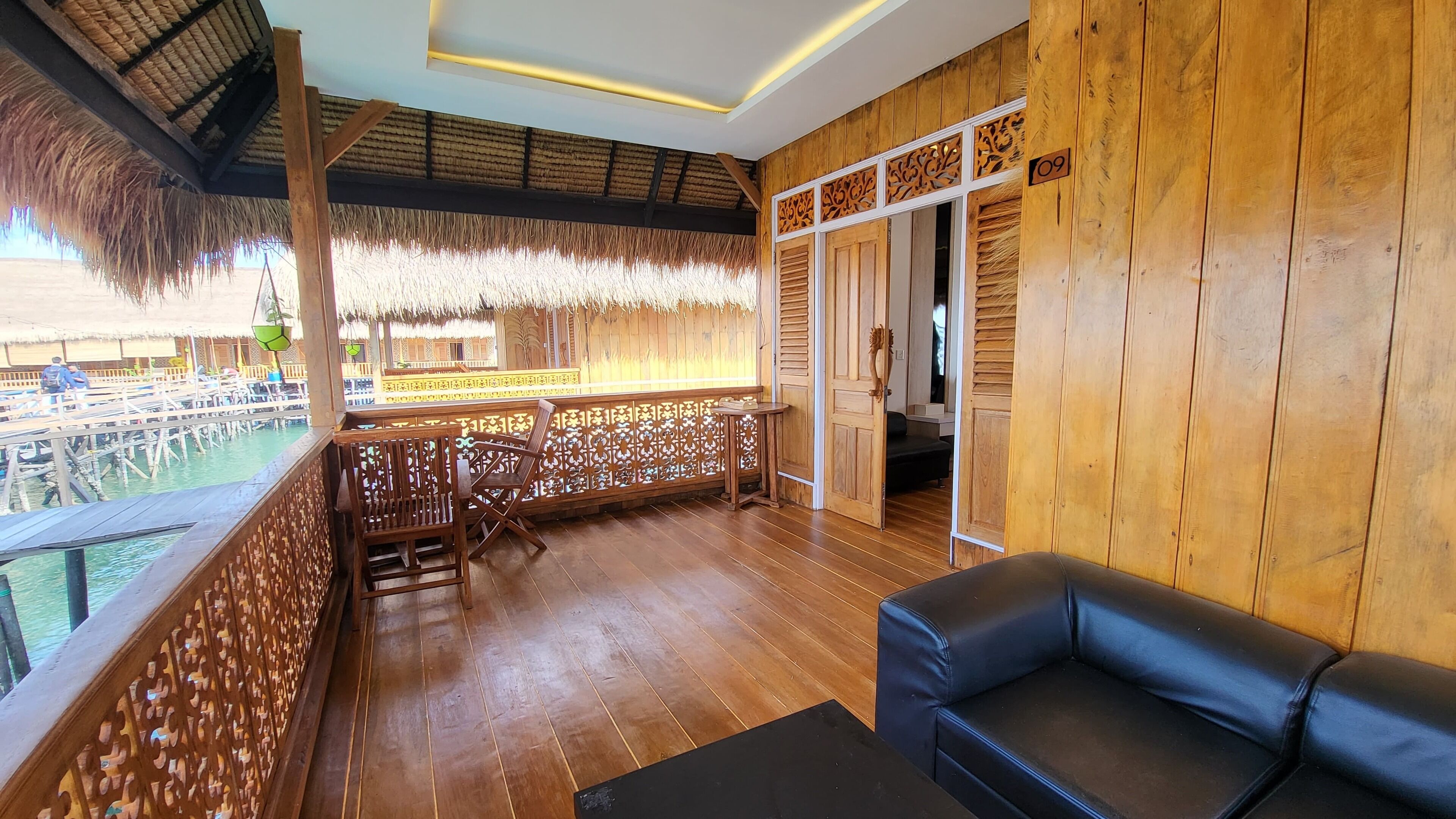 A wooden interior with a wooden floor, a black leather sofa, and a thatched ceiling.