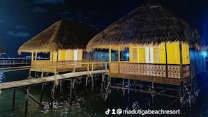 Overwater bungalows with thatched roofs and wooden railings, connected by a wooden walkway over water.