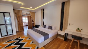 A modern bedroom with a large bed, a desk, and a chair. There is a window with curtains and a view of the outdoors.