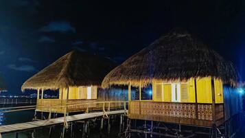 Bungalows sobre el agua con techos de paja y barandillas de madera, unidos por una pasarela de madera sobre el agua.