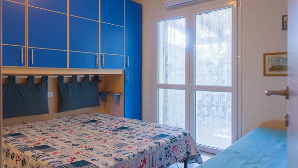 Een kamer met een bed, een raam met uitzicht en blauwe kasten.