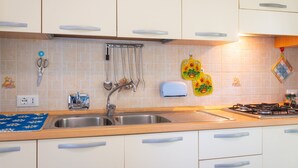 A kitchen with white cabinets, a stainless steel sink, a gas stove, and a variety of kitchen utensils and appliances. - Apartment with garden in Lacona, ideal for relax. (Capoliveri)
