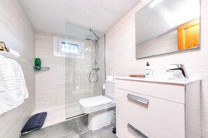 Et moderne badeværelse med en glas brusekabine, toilet, håndvask med spejl og et håndklædetørrestativ.
