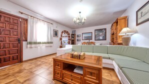 Een gezellige woonkamer met een houten salontafel, een groen geruit bankstel, een houten kast en een kroonluchter.