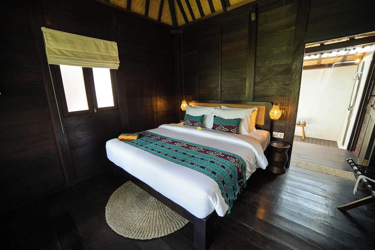 A wooden room with a bed, a small table, and a window with a blind.