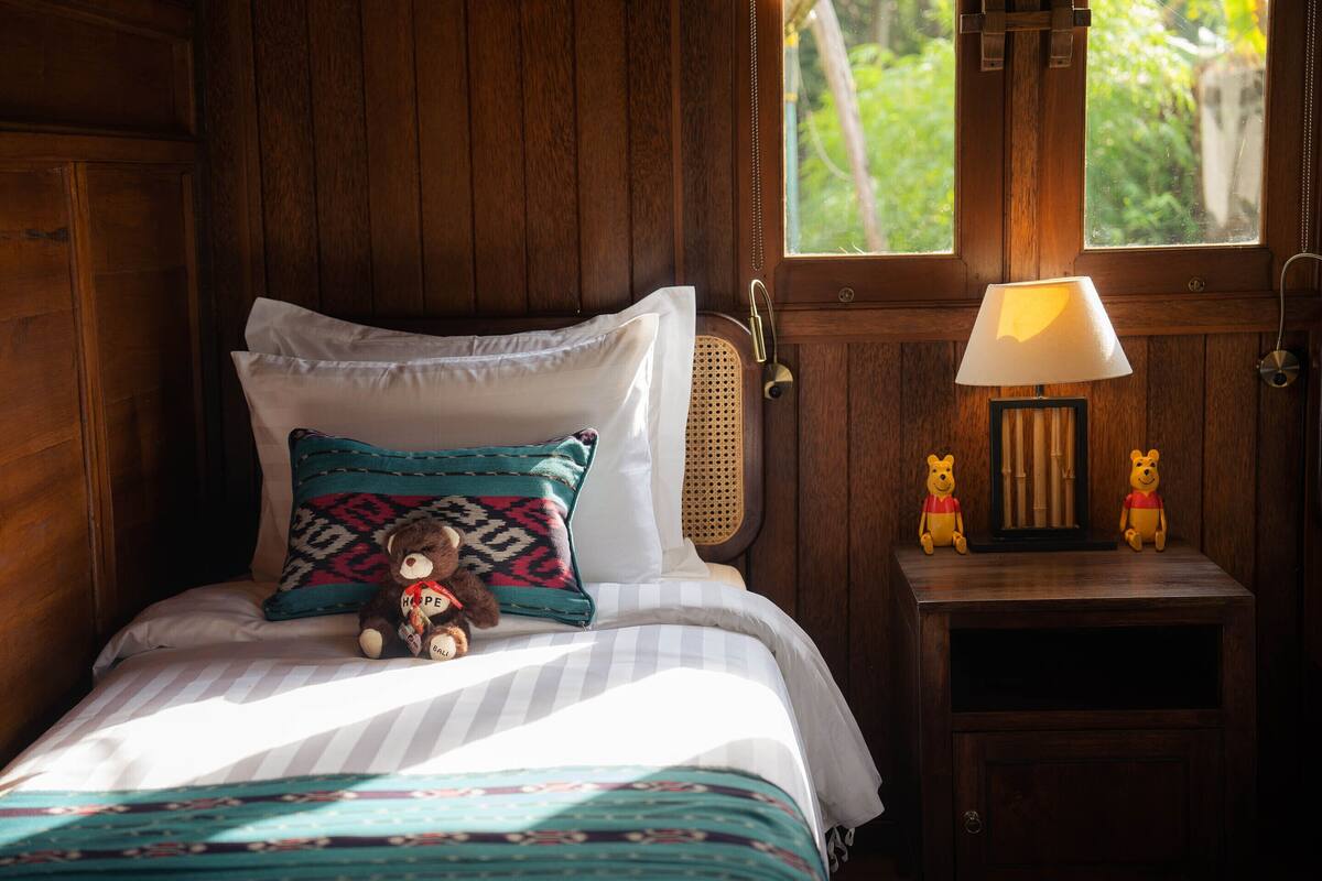 A wooden-paneled room with a bed, a bedside lamp, and two teddy bears on a nightstand.