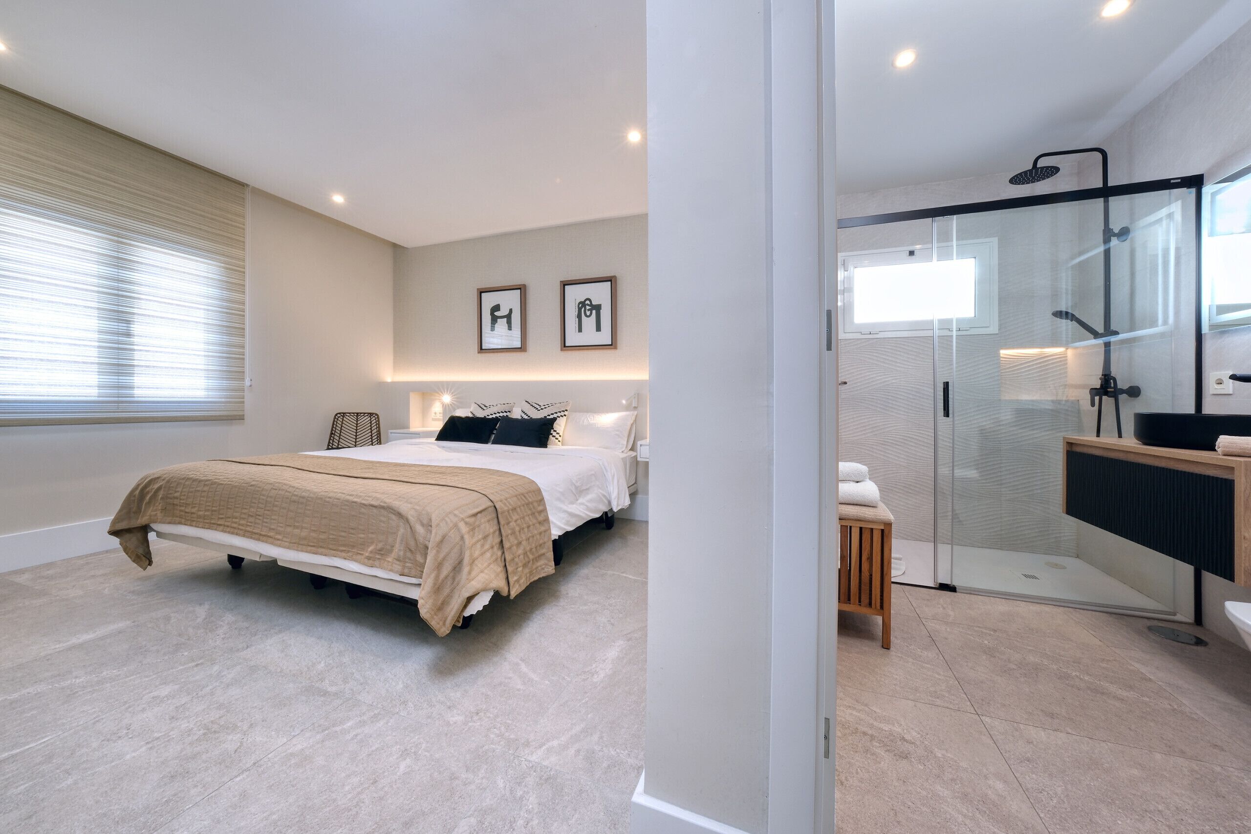 A modern bedroom with a bed, bedside tables, and a large window with blinds.