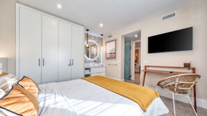 Ein Schlafzimmer mit Bett, Kleiderschrank, Schminktisch, Spiegel, Fernseher und einem Sessel.