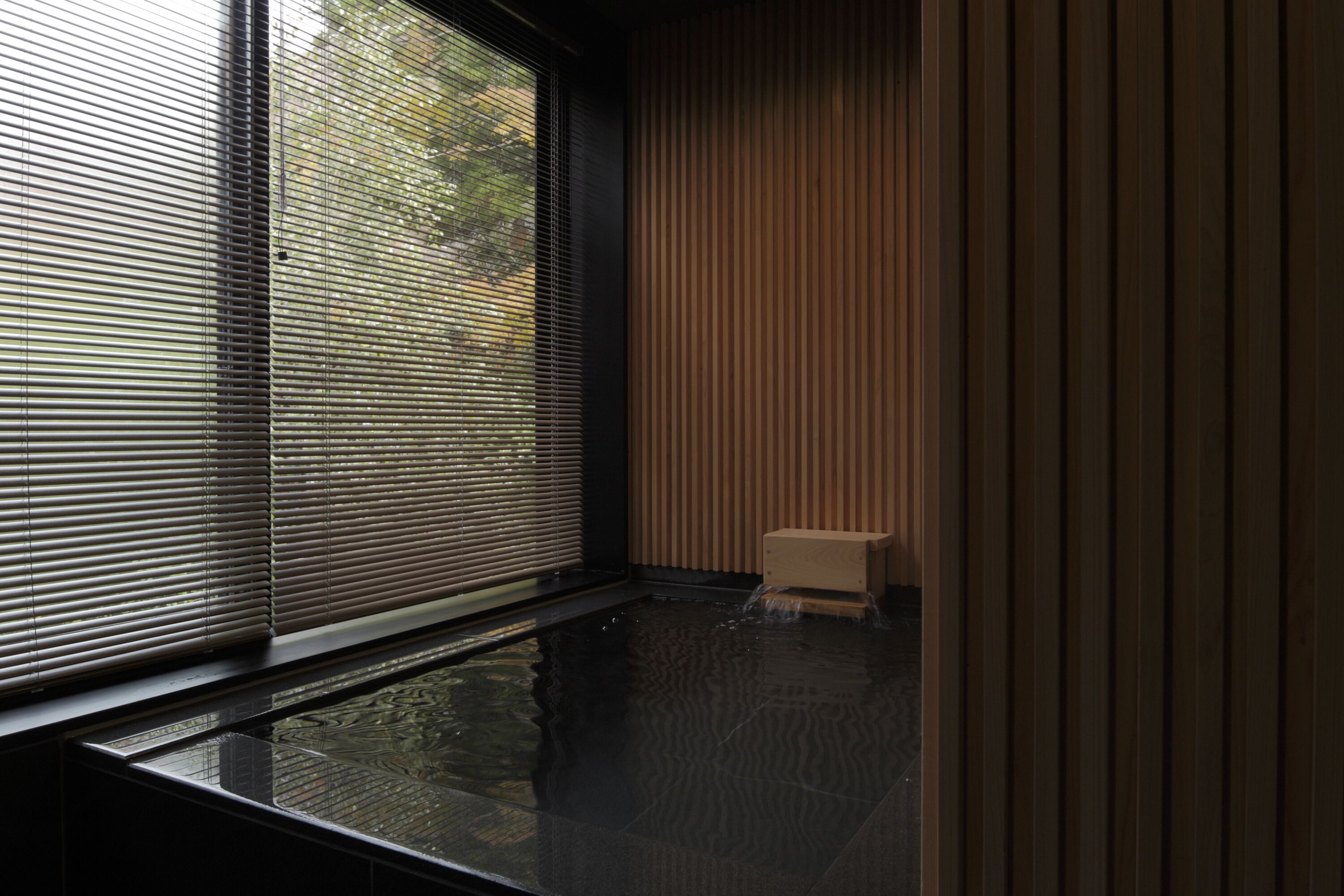 A room with a large window, a small wooden stool, and a water feature.