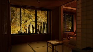 Una habitación japonesa tradicional con suelo de tatami, una mesa baja y un ventanal con vistas a árboles otoñales.