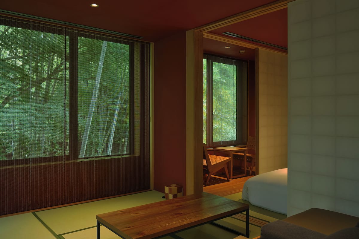 Une pièce de style japonais traditionnel, avec un sol recouvert de tatamis, une petite table en bois et un lit doté d’un matelas blanc.