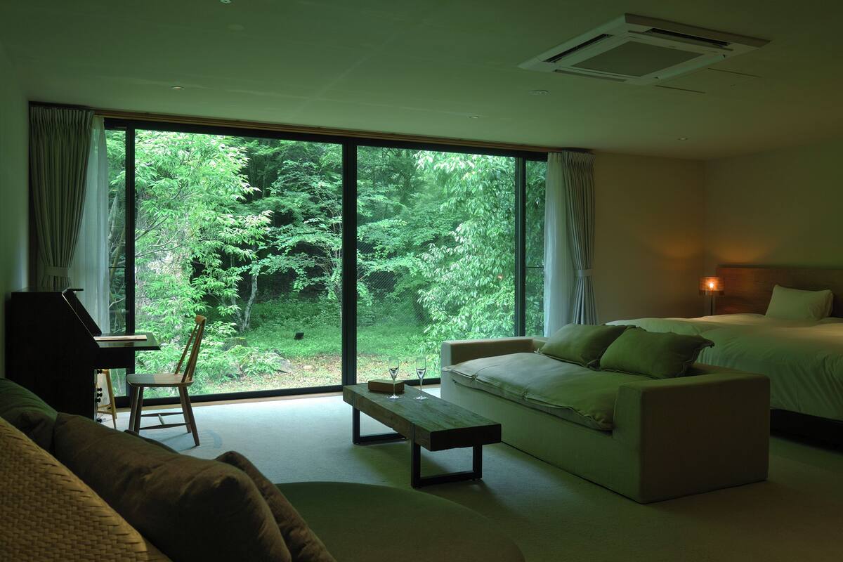 Une chambre avec une grande fenêtre, un lit, un canapé, une chaise et une petite table avec des verres.