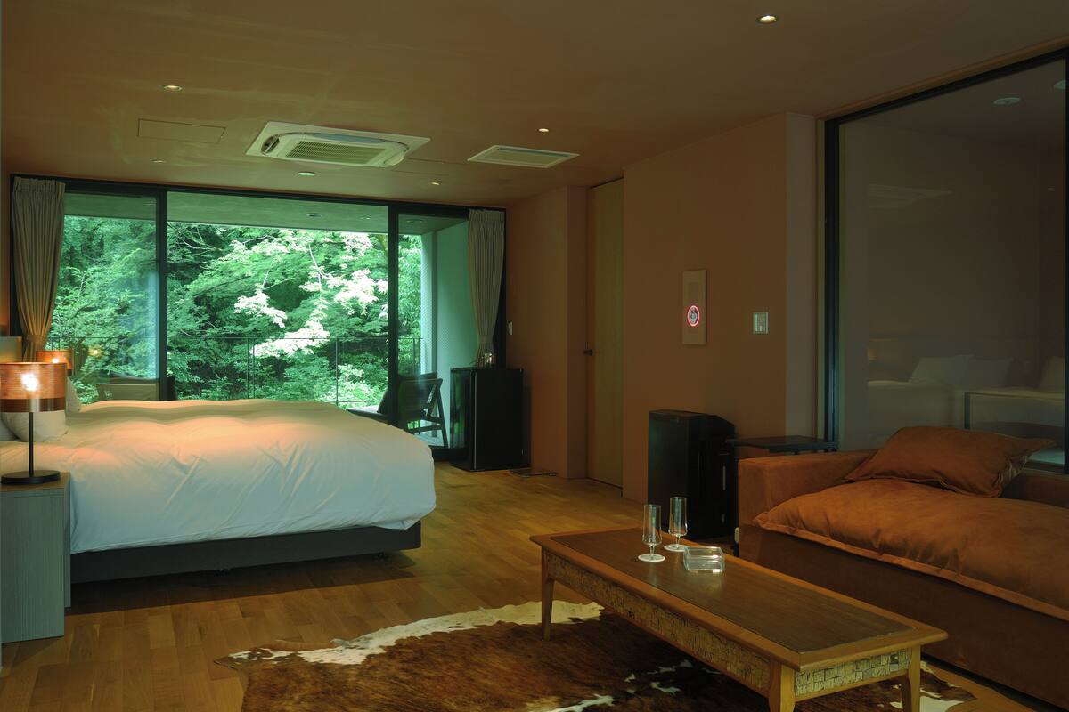 Une chambre moderne avec un grand lit, une table basse en bois et une vue sur la verdure grâce à de grandes fenêtres.