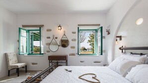 Una camera da letto con un letto, due finestre, una sedia, uno specchio e una lampada a sospensione.