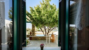 Una finestra aperta con vista su un patio arredato con tavolo, sedie e una pianta in vaso.