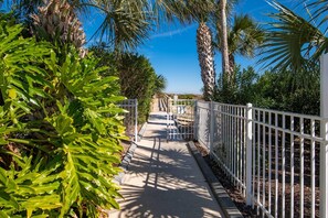 A pathway flanked by white fences and lush greenery, leading to a gated entrance. - Stunning Ocean Views, Beachfront Pool, Heated Indoor Pool, Hot Tub, Family Condo, Tennis, Gym, Sauna (St. Augustine)