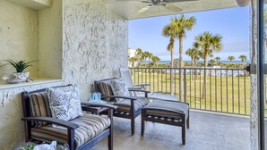 A balcony with two cushioned chairs and a table, a ceiling fan, and a view of palm trees and the ocean. - Stunning Ocean Views, Beachfront Pool, Heated Indoor Pool, Hot Tub, Family Condo, Tennis, Gym, Sauna (St. Augustine)