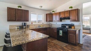A modern kitchen with granite countertops, dark wooden cabinets, a black stove, and a window providing a view of the outdoors.