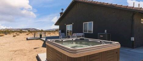Una casa con jacuzzi en el patio trasero, un porche con mobiliario exterior y una vista despejada del paisaje circundante.
