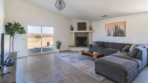 A spacious living room with a large gray sectional sofa, a fireplace, and a view through a sliding glass door to an outdoor area.