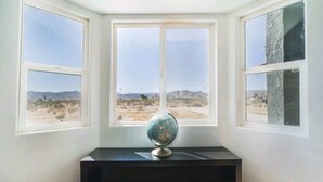 A room with a desk and a globe, three windows with a desert view, and a stone wall.
