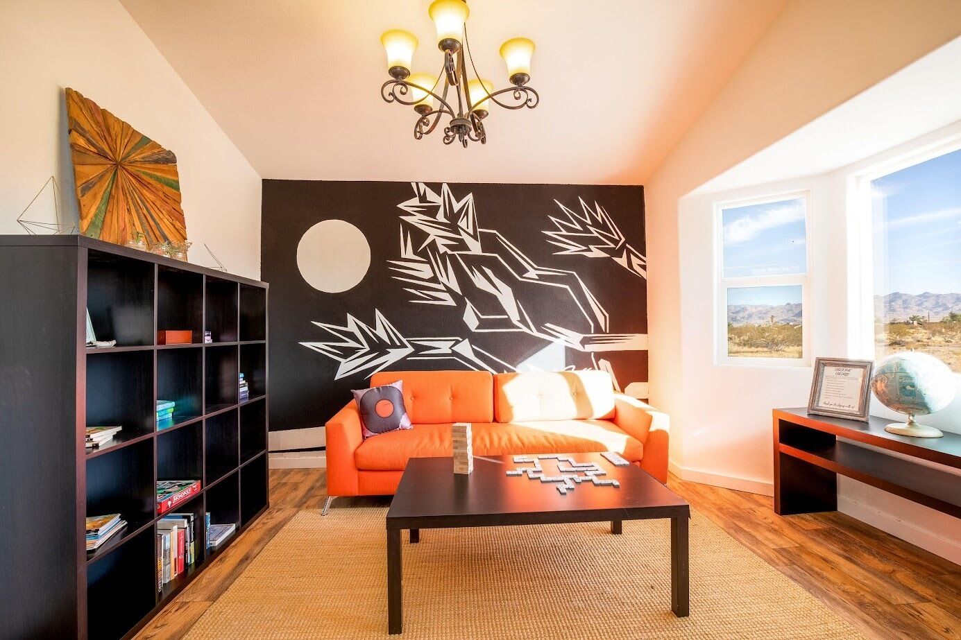 Un salon moderne avec un canapé noir et orange, une bibliothèque, une table basse et une fresque murale.