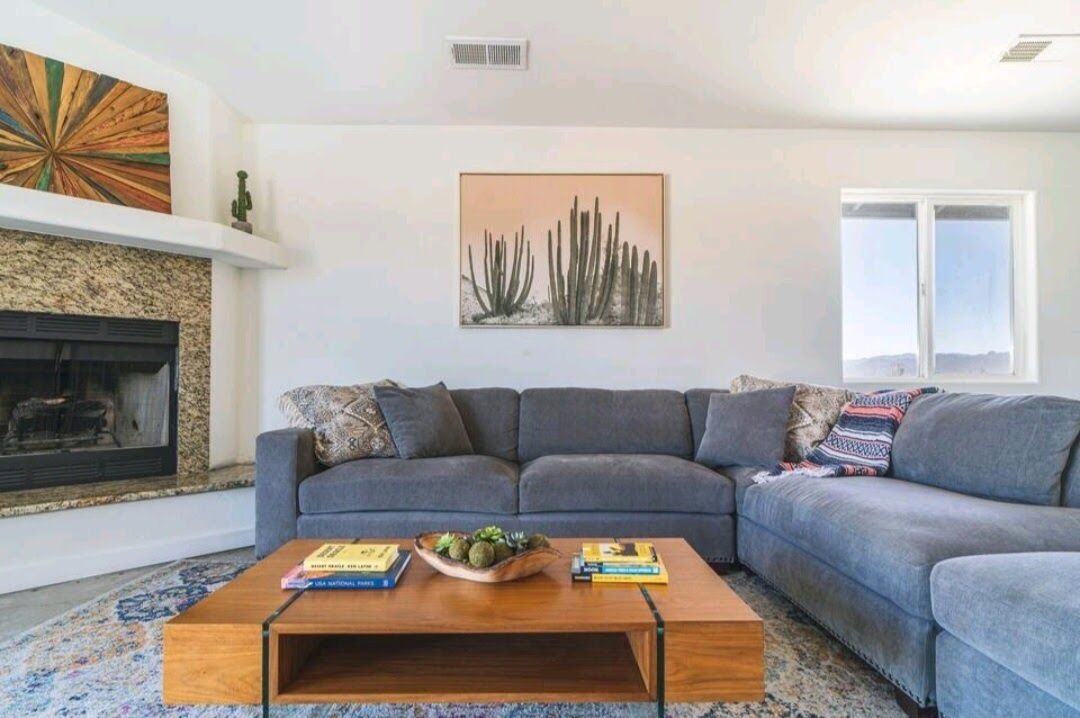 A living room with a gray sectional sofa, a wooden coffee table, a fireplace, and a cactus painting on the wall.