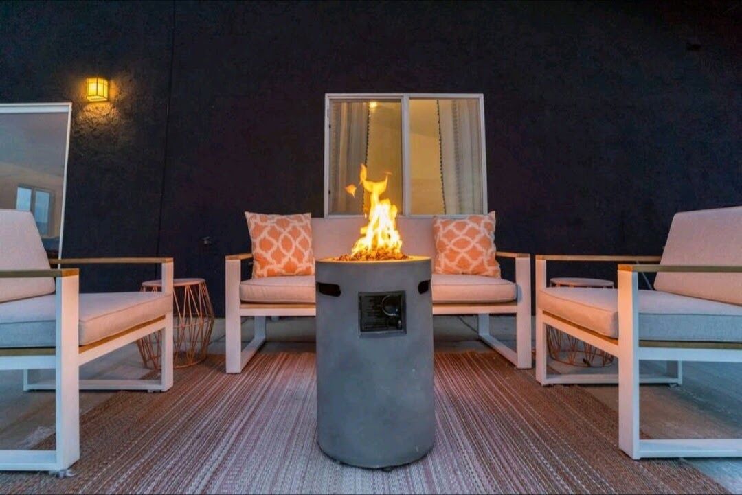 Ein Patio mit Feuerstelle in der Mitte, gepolsterten Sitzgelegenheiten und einem Fenster mit Vorhängen.