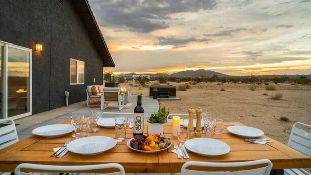 An outdoor dining area with a table set for four, surrounded by desert landscape and mountains in the background.
