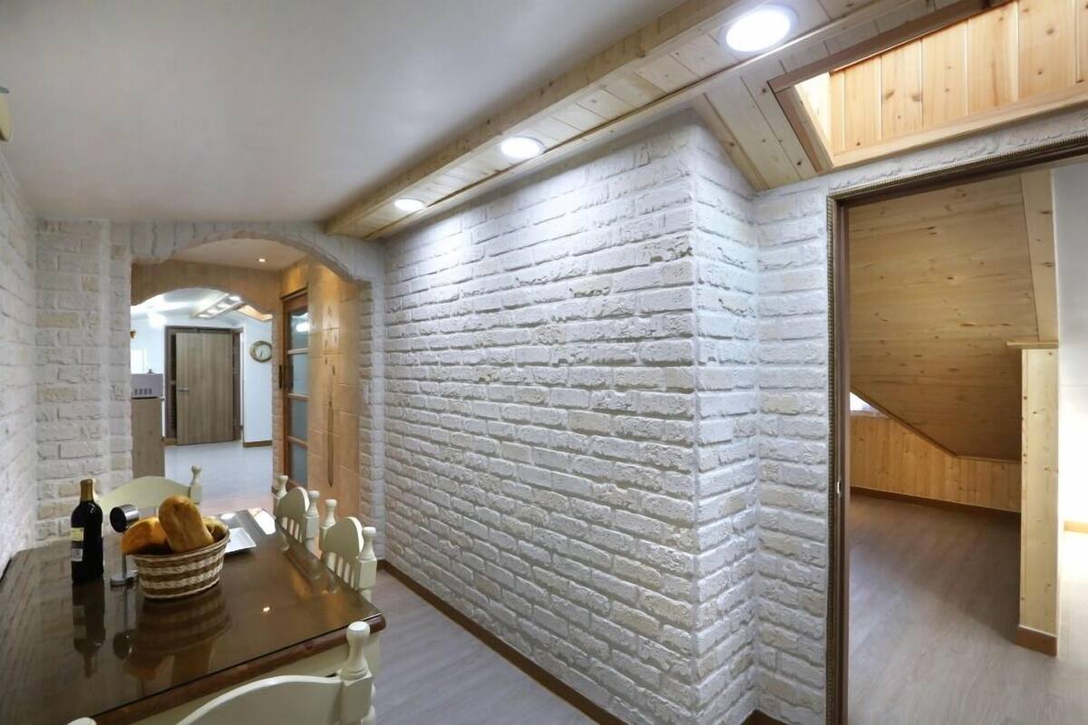 A dining area with a brick wall, wooden ceiling beams, and a view into another room.