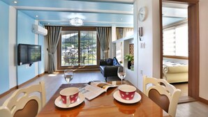 A hotel room with a dining table set for two, a sofa, a TV, and a view of the outdoors. - Monami Pension (Tongyeong)
