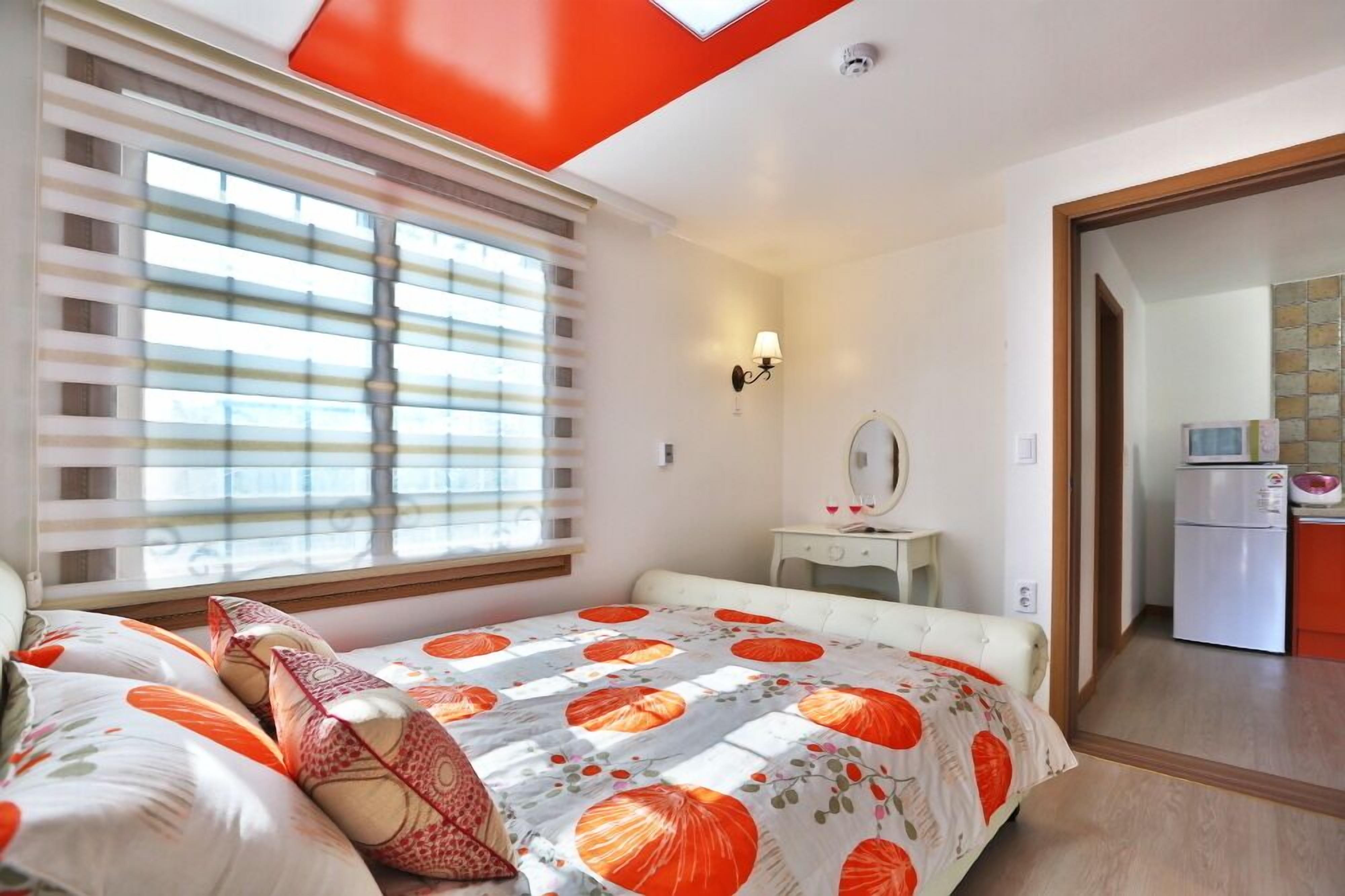 Un dormitorio con cama, mesita de noche, espejo y ventana con persianas.