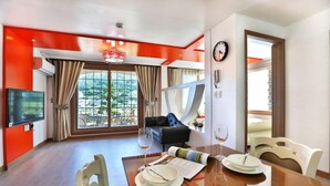 A modern dining area with a wooden table set for two, a black sofa, and a large window with curtains. - Monami Pension (Tongyeong)