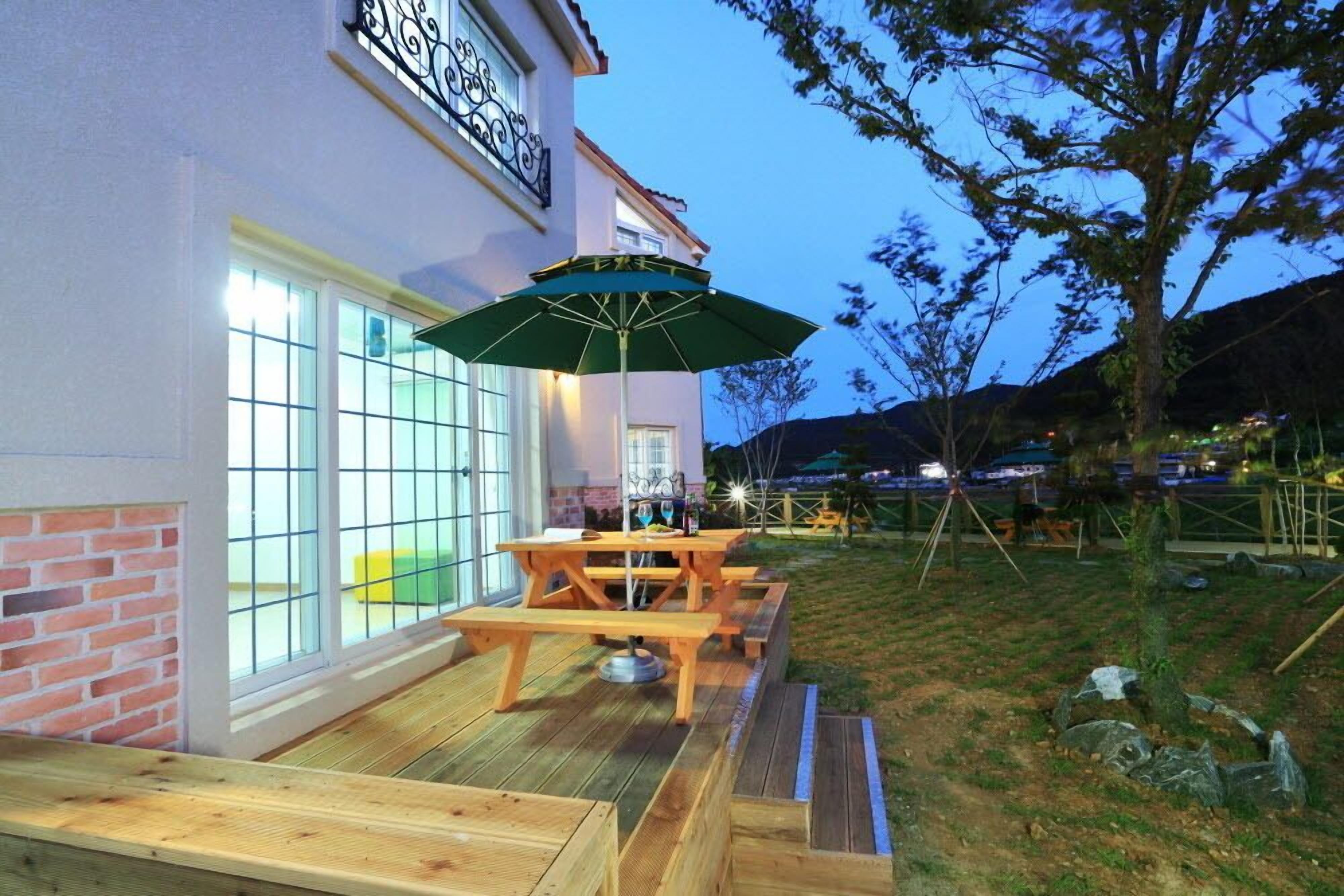 Un área de patio con bancos de madera, una mesa, un paraguas verde y un muro de ladrillo.