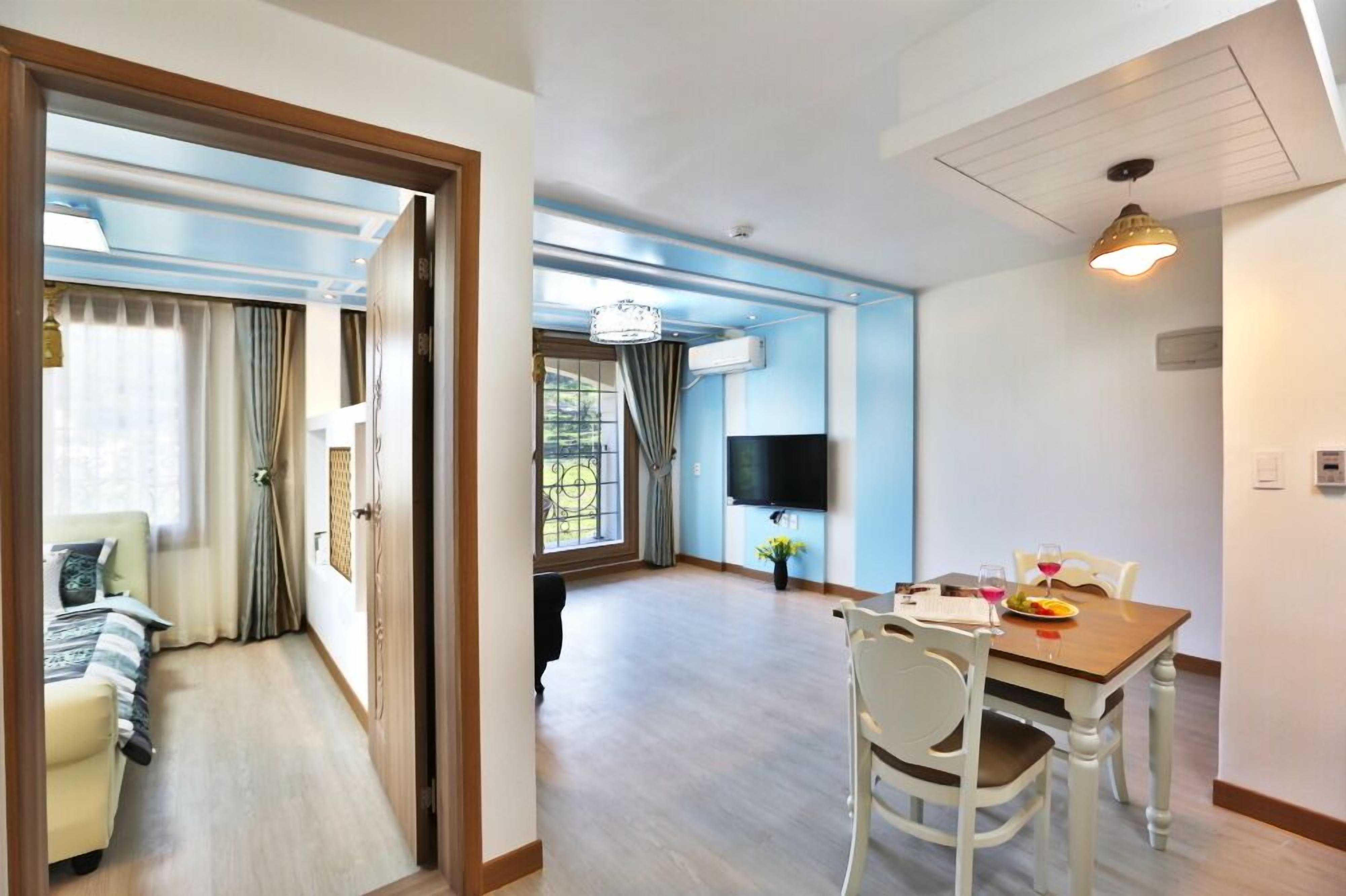 Une chambre d’hôtel comprenant un lit, un coin repas avec une table et des chaises, une télévision et une fenêtre avec des rideaux.