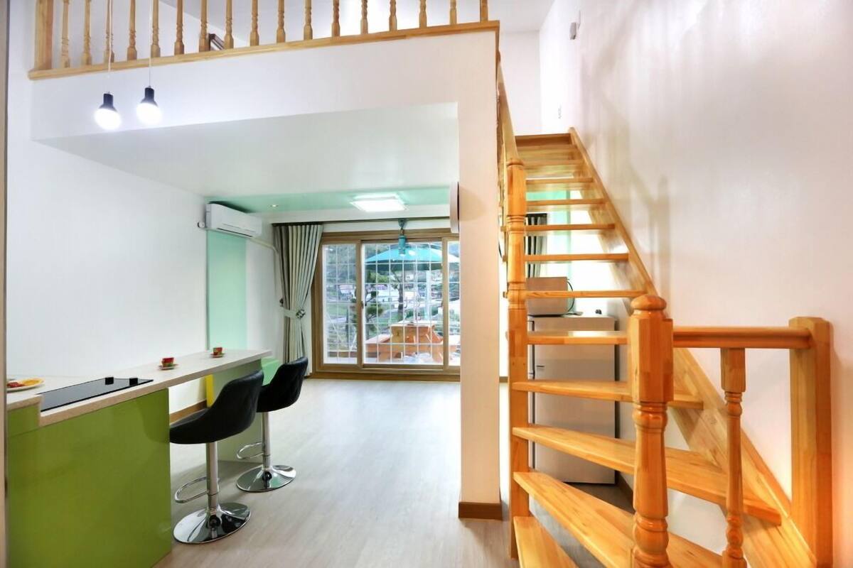 A modern apartment with a kitchen area, a dining space with two chairs, a staircase, and a large sliding glass door leading to a balcony.