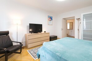 A bedroom with a bed, a TV on a dresser, a chair, and a floor lamp.