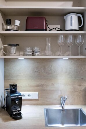 Une cuisine équipée d’une machine à café, d’une bouilloire et de verres à vin rangés sur une étagère.