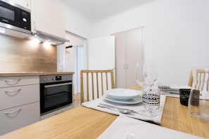 A modern kitchen with a dining table set for two, featuring white plates, glasses, and cutlery.