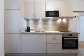 Une cuisine moderne avec des meubles de couleur claire, un évier en acier inoxydable, un four à micro-ondes et un four traditionnel.