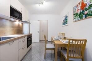 A compact kitchen with a microwave, oven, and wooden countertop. There is a dining table with chairs and a door leading to another room.