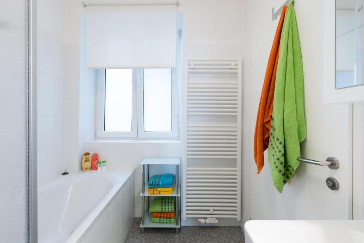 Ein Badezimmer mit einer Badewanne, einem Fenster, einem Handtuchhalter mit Handtüchern und einem Regal mit gefalteten Handtüchern.